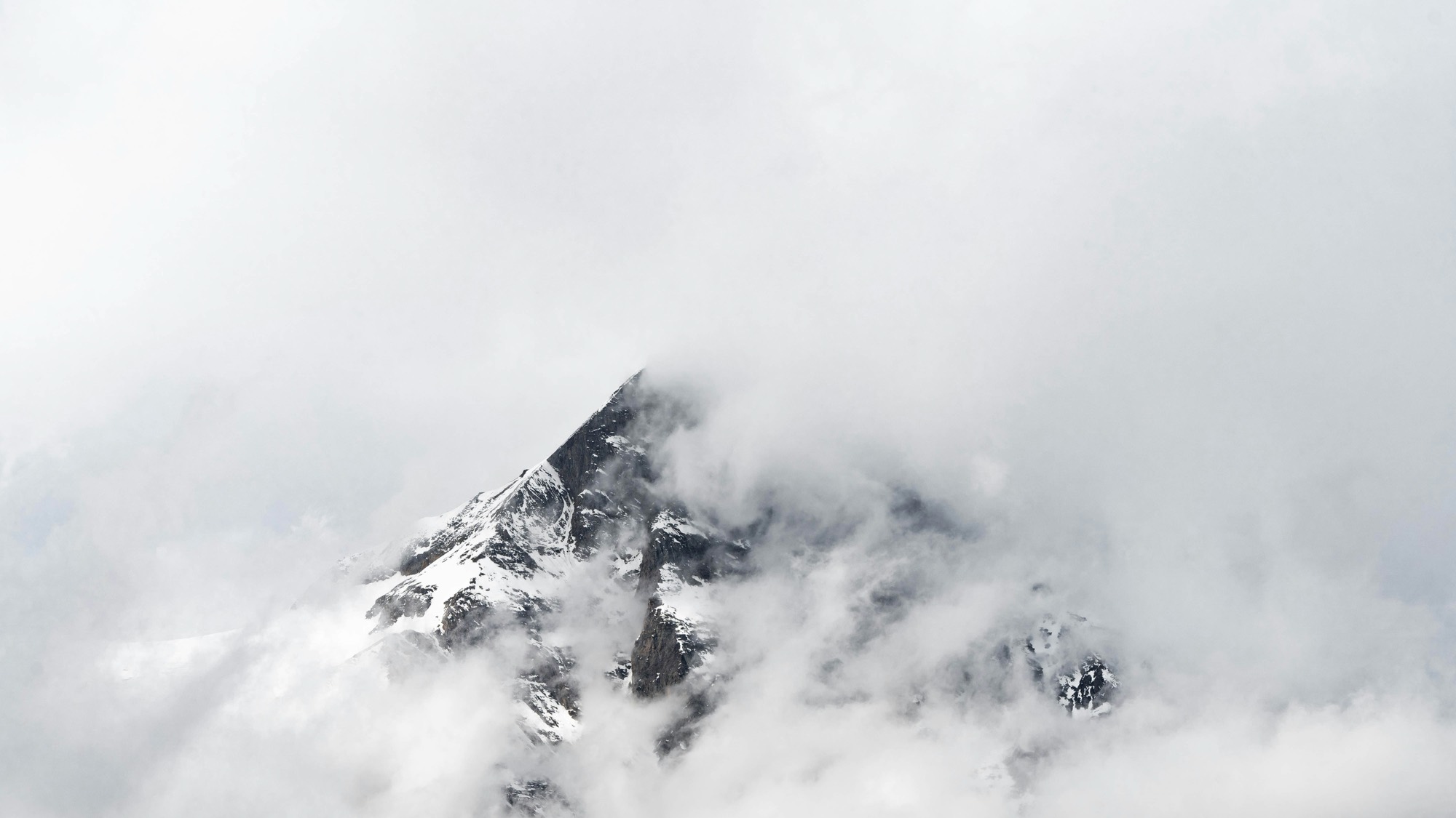 A snow-covered alpine peak emerging from clouds